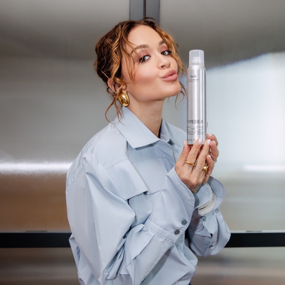 Frau mit hellbraunem, lockigem Haar hält eine silberne Dose Trockenshampoo der Marke Typedbea G.5 in der Hand.
