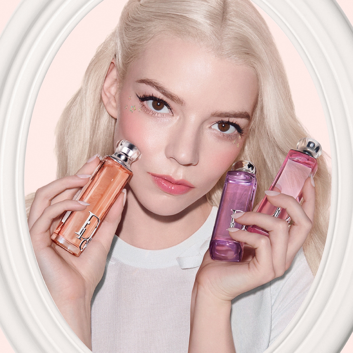 Entdecken Sie die Dior Duftkollektion, präsentiert von einem blonden Model mit Sternen-Make-up, das drei Flakons in Pfirsich-, Lila- und Rosatönen hält.