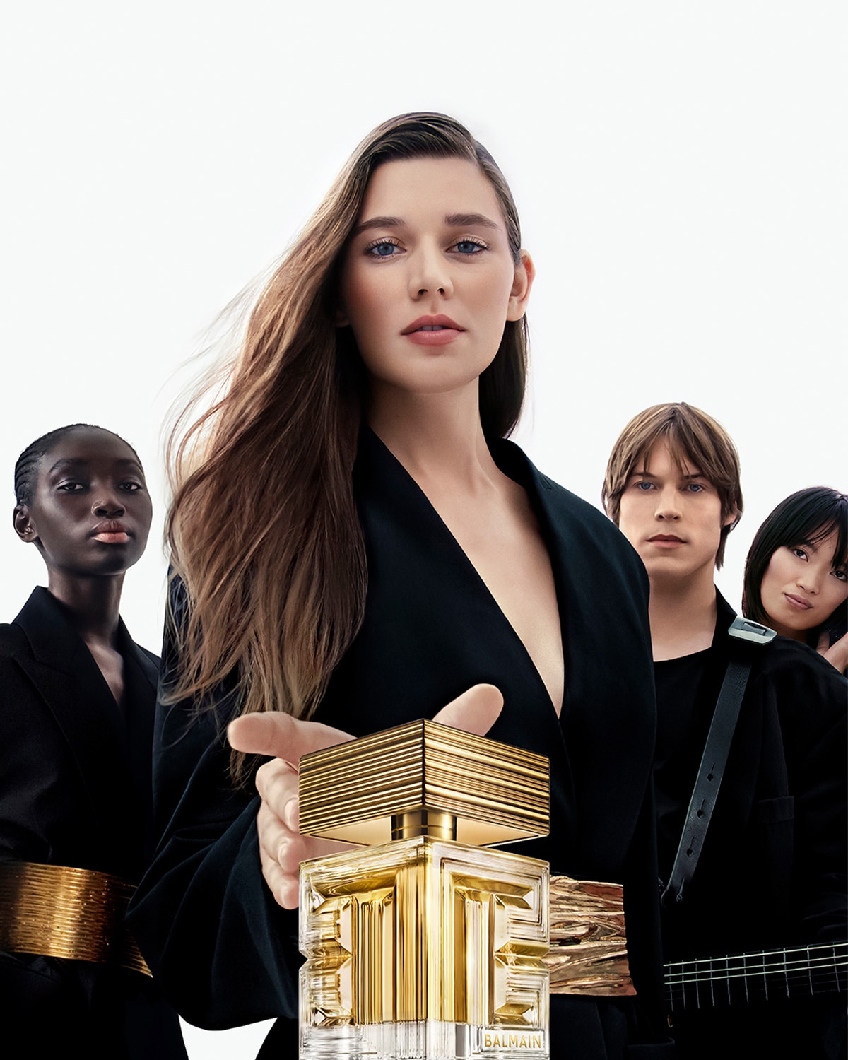 D'Balmain Parfumfläsch steet am Virdergrond, mat engem gëllenen Design, ëmgi vun enger Grupp vu Leit a schwaarzer Kleedung, déi Eleganz a Stil ausstrahlen.
