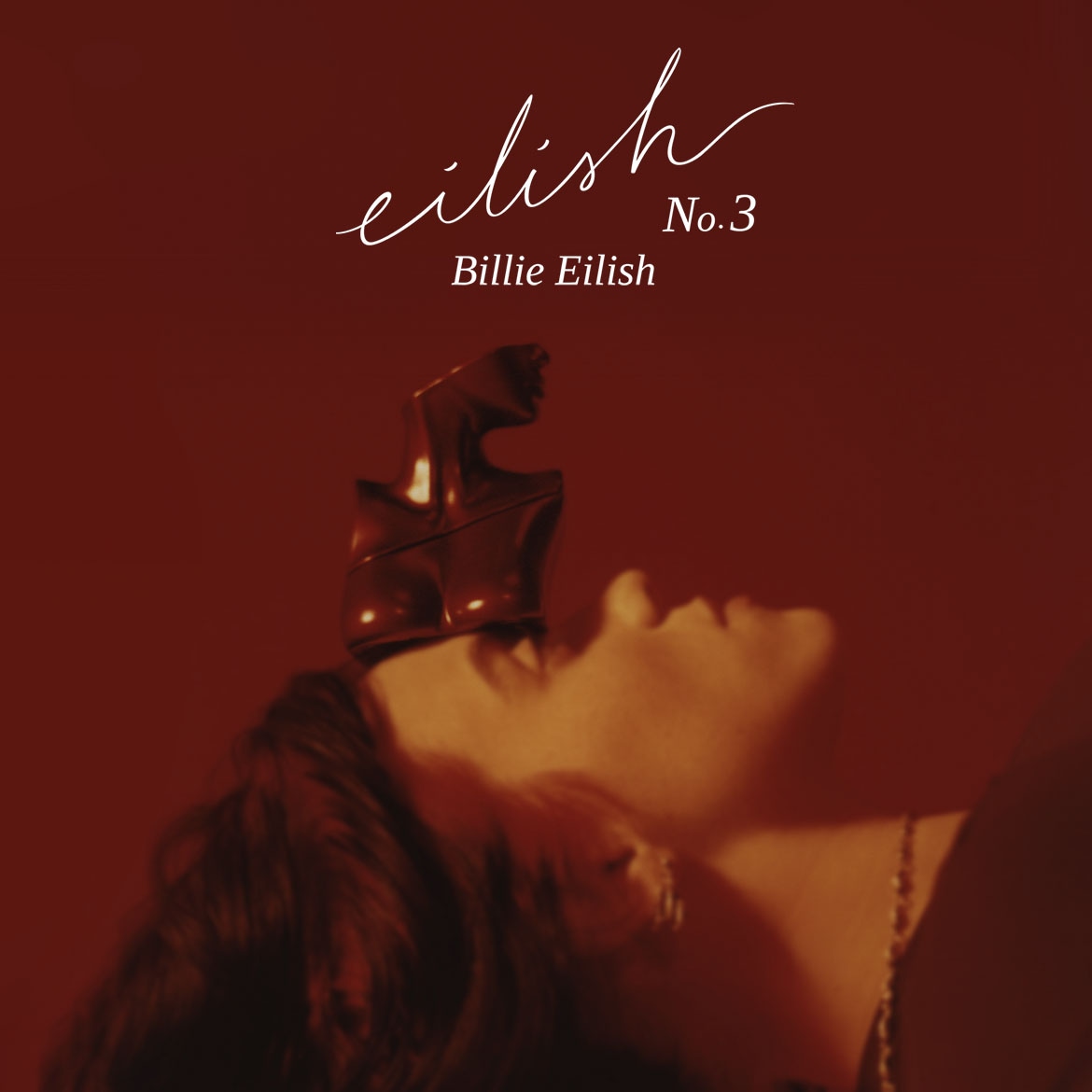 Das Bild zeigt Billie Eilish No. 3 Duft mit einer Frau, die eine bronzefarbene Oberkörperstatue auf dem Kopf trägt, vor einem roten Hintergrund.