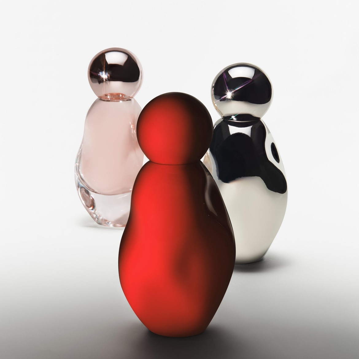Drei Flakons in Rot, Rosa und Schwarz-Weiss stehen auf einem hellen Untergrund, die wie stilisierte Figuren wirken.