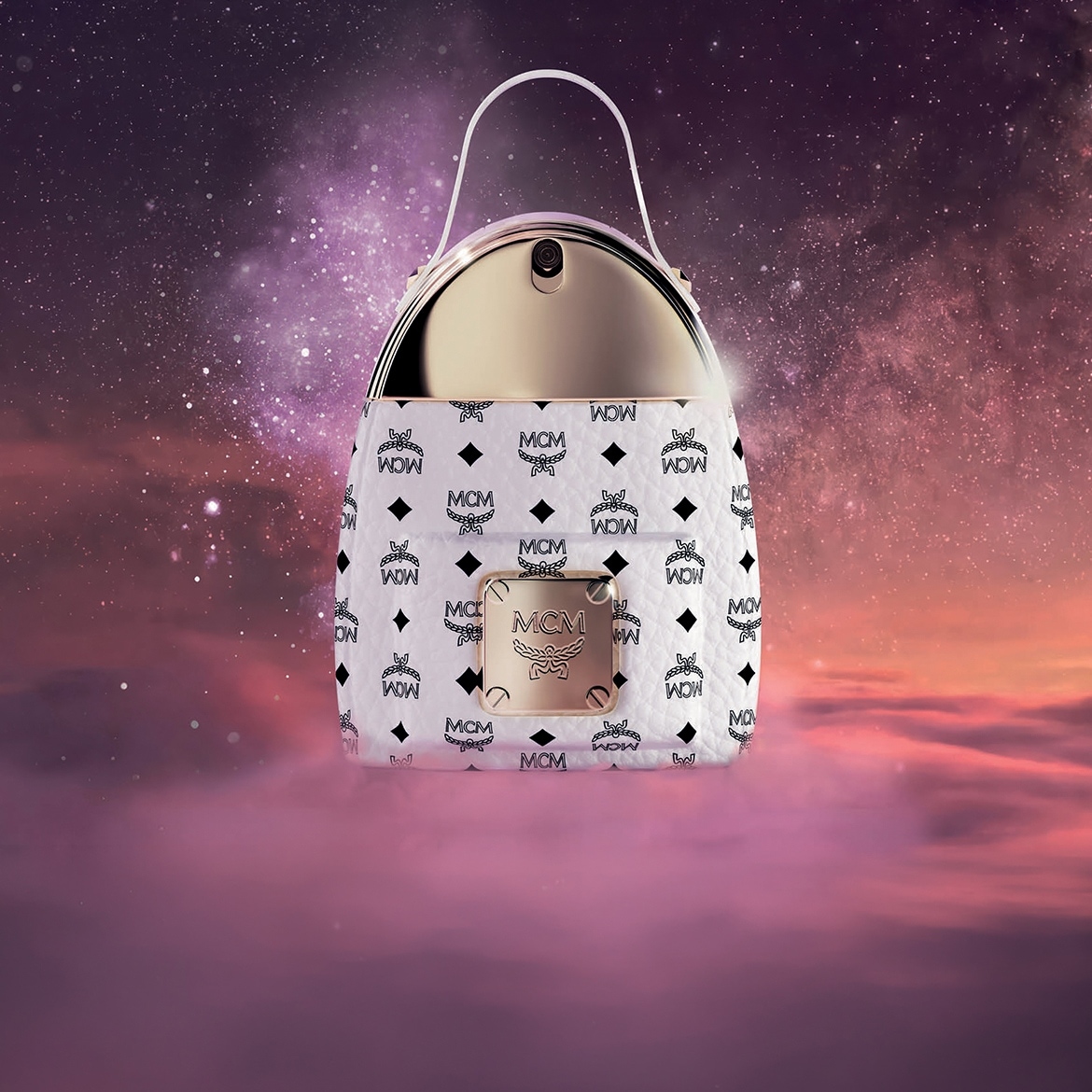 Der MCM Eau de Parfum Flakon in Form einer weissen MCM-Tasche mit goldenen Akzenten und Griff, vor einem lila-rosa Himmel mit Sternen.