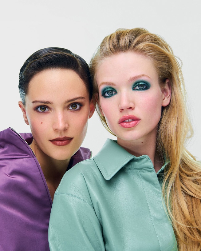 Zwei Personen präsentieren unterschiedliche herbstliche Make-up-Looks vor hellem Hintergrund. Die Aufnahme steht für saisonale Beauty-Trends, von warmen Naturtönen bis zu ausdrucksstarken Farbakzenten.