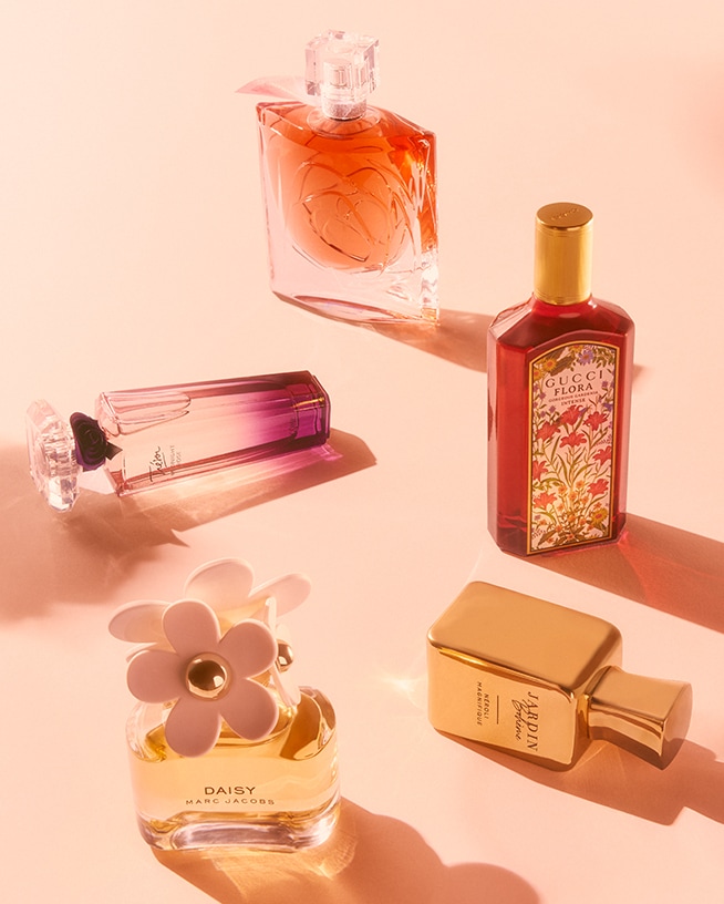 Eine Kollektion von Damendüften, darunter Lancôme Trésor, Gucci Flora, Marc Jacobs Daisy und Jardin Bohème, präsentiert in eleganten Flakons auf einem sanften, rosafarbenen Hintergrund