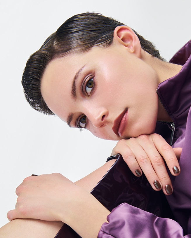 Nahaufnahme einer Person mit herbstlichem Make-up und dunklem Nagellack vor hellem Hintergrund. Die Aufnahme steht für saisonale Make-up-Trends und Beauty-Inspirationen für den Herbst.