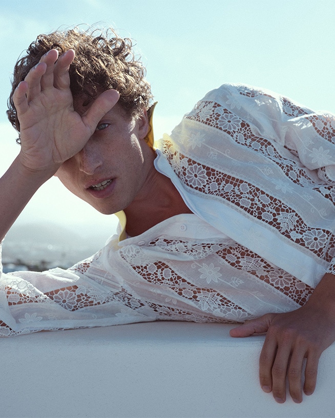 Un homme se protège du soleil avec sa main, portant une chemise blanche en dentelle, soulignant l'importance de la protection solaire.