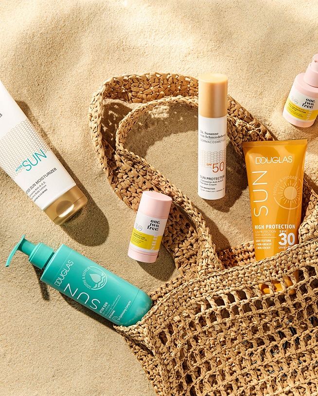 Une collection de produits de protection solaire, comprenant des lotions après-soleil et des écrans solaires avec différents FPS, présentés dans un sac de plage sur le sable.