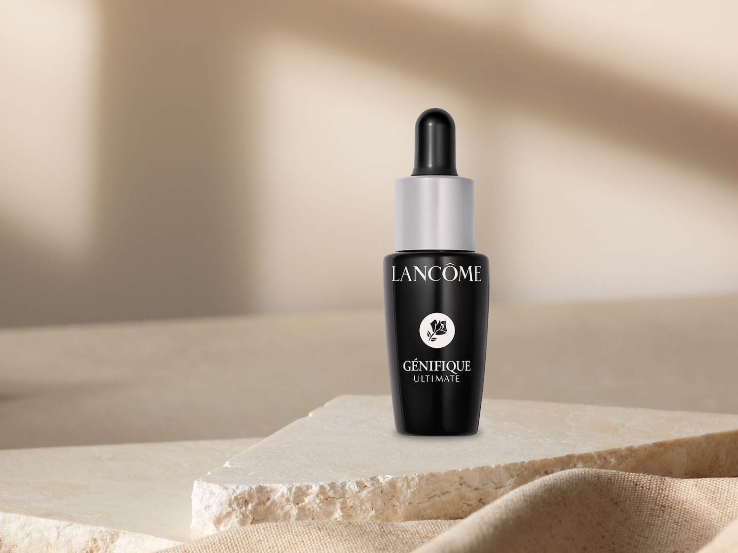 Schwarze Lancôme Génifique Ultimate Flasche mit Pipette auf einem beigen Untergrund, die als Geschenk angeboten wird.