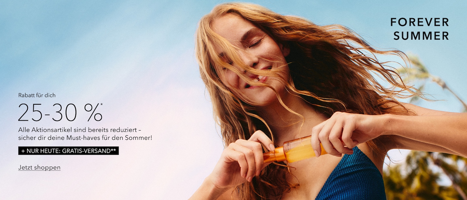 Eine junge Frau mit langen, gewellten blonden Haaren, die ihr Gesicht teilweise bedecken, hält eine orangefarbene Flasche mit Sonnenöl in der Hand, während sie in einem blauen Oberteil vor einem hellblauen Himmel lächelt.