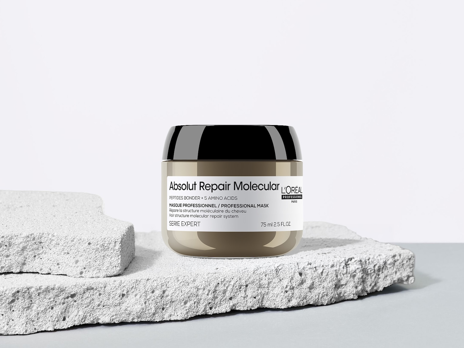 Die L'Oréal Professionnel Absolut Repair Molecular Maske in einem beigen Tiegel mit schwarzem Deckel, der 75 ml des Produkts enthält, steht auf zwei grauen, strukturierten Blöcken.