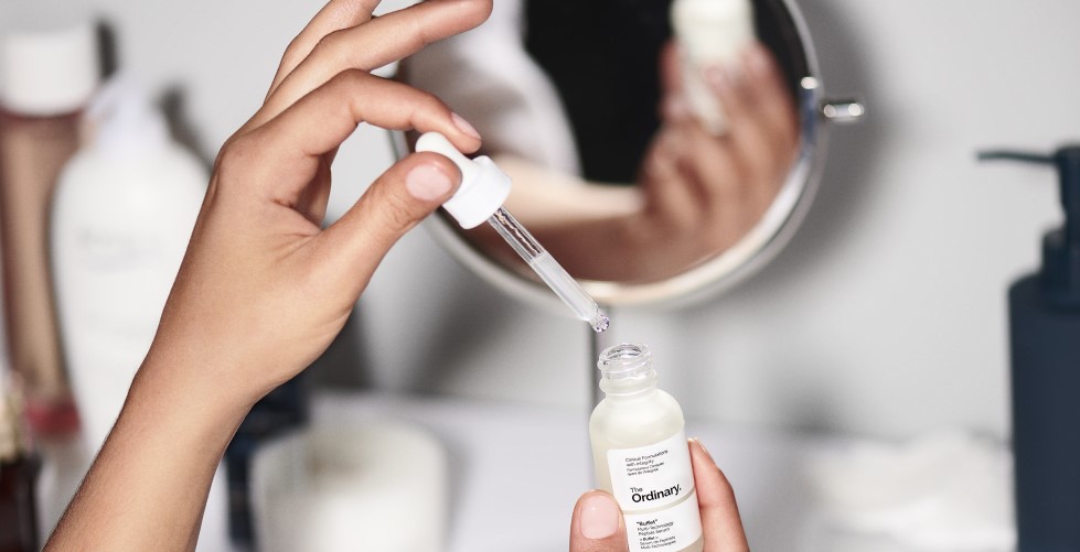 D'Hänn hält eng Pipette iwwer eng Fläsch The Ordinary "Buffet" + Copper Peptides 1% Serum, fir d'Hautpfleeg ze verbesseren.