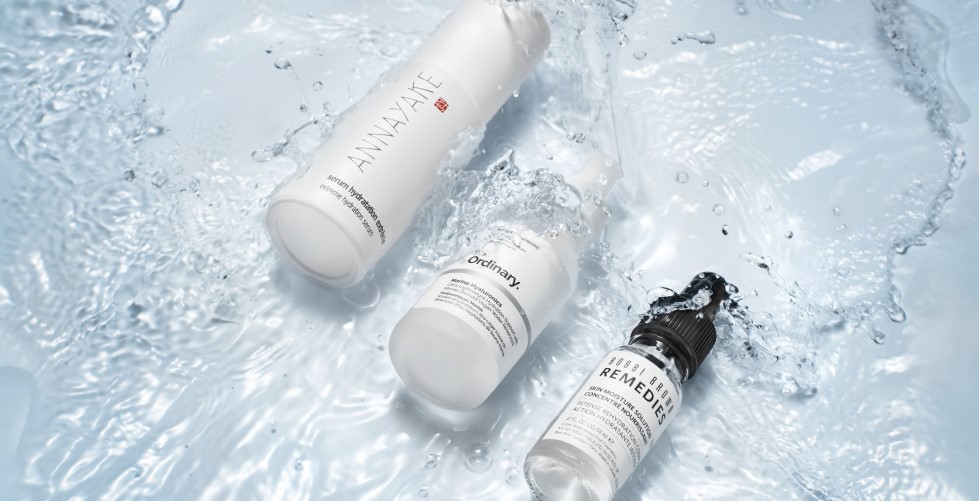 Drei weiße Hautpflegeprodukte von Annayake, The Ordinary und Bobbi Brown Remedies liegen im Wasser, umgeben von Spritzern, die ihre feuchtigkeitsspendenden Eigenschaften hervorheben.