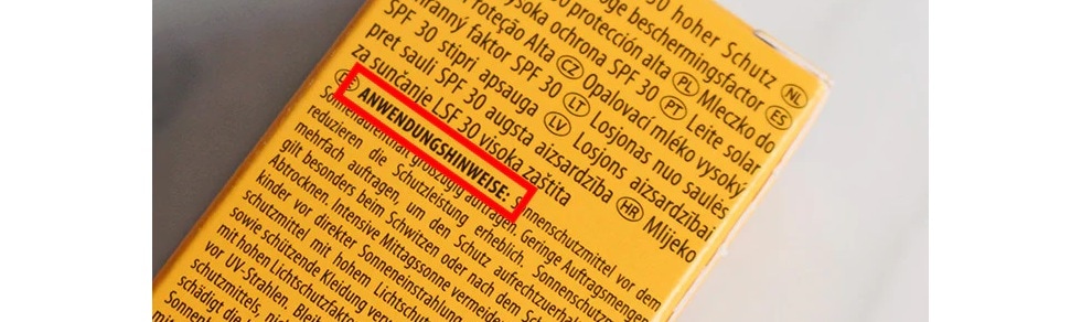 Auf der gelben Verpackung des Sonnenschutzmittels sind Anwendungshinweise in verschiedenen Sprachen aufgedruckt, darunter Deutsch, mit dem Hinweis, das Produkt grosszügig aufzutragen.
